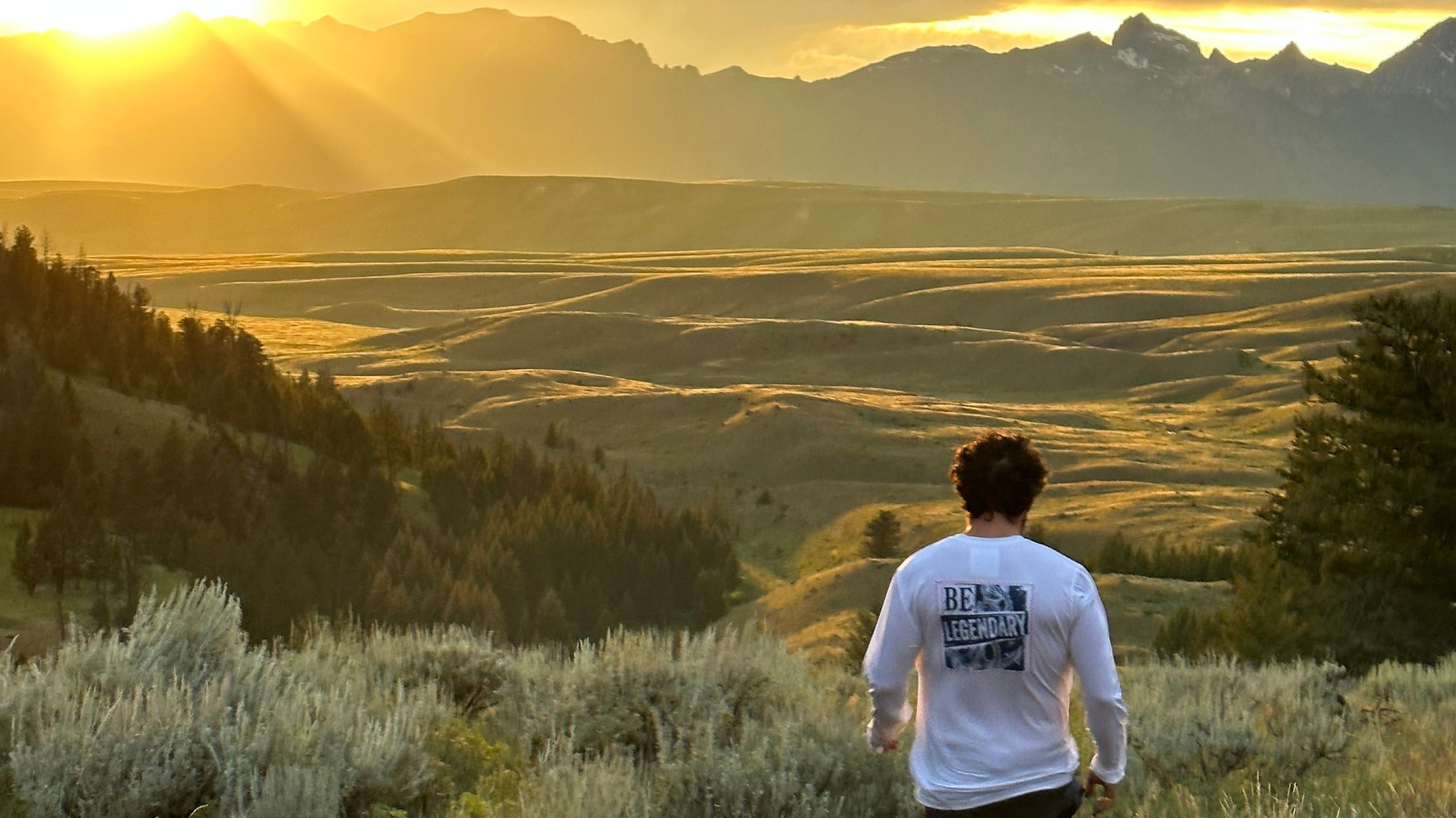 man in shorts and long sleeve tee walking through a beautiful Wyoming field at sunset