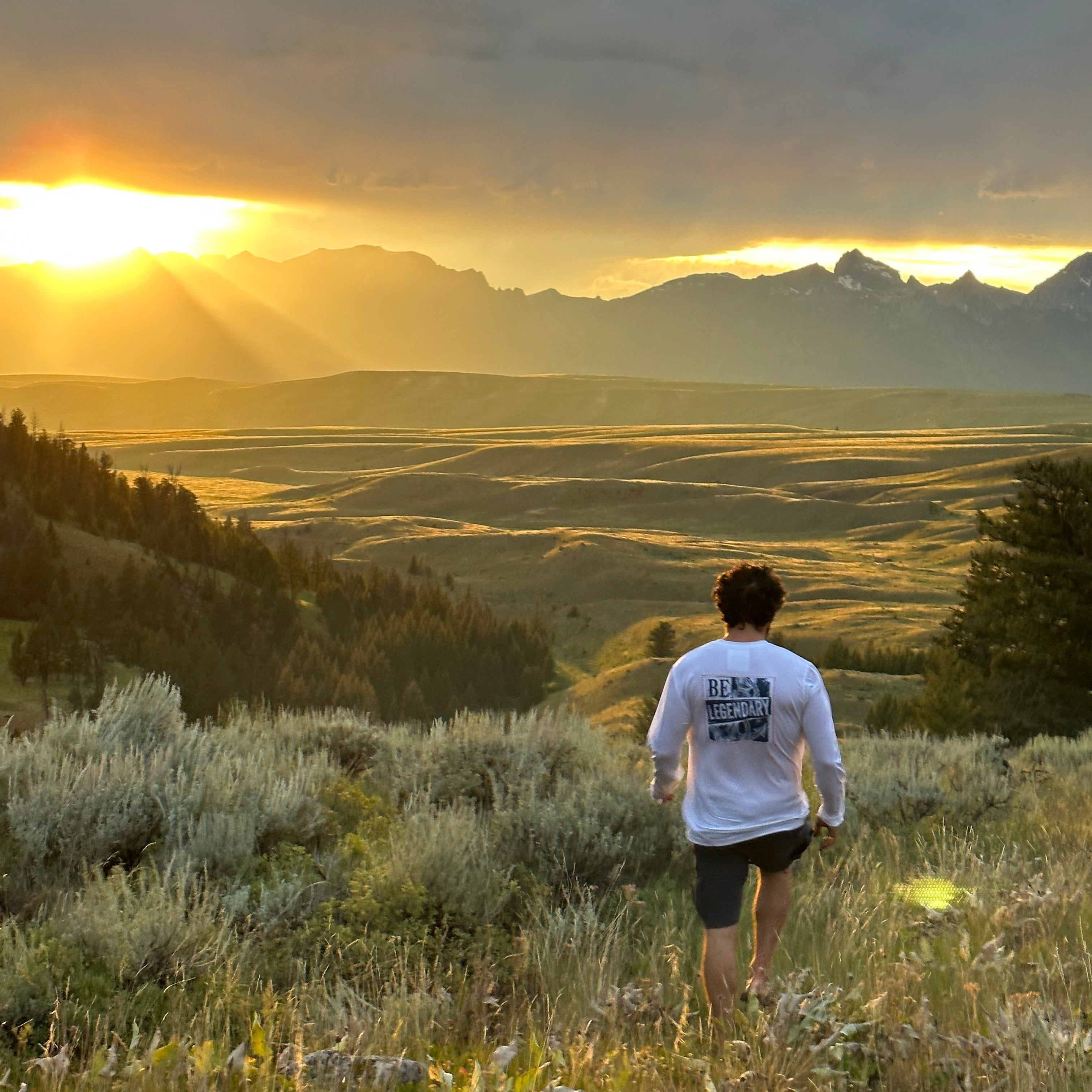 man in shorts and long sleeve tee walking through a beautiful Wyoming field at sunset