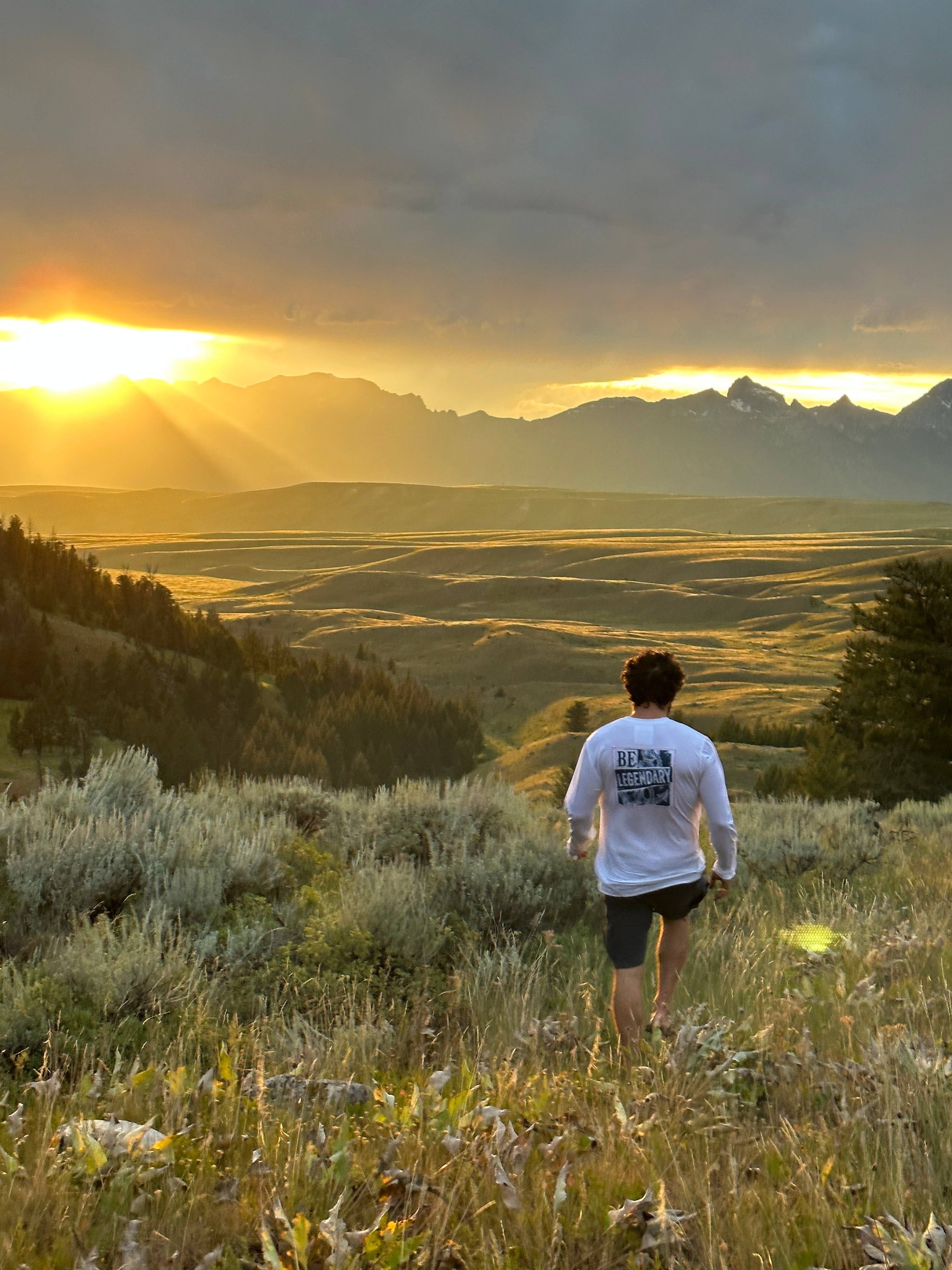 man in shorts and long sleeve tee walking through a beautiful Wyoming field at sunset